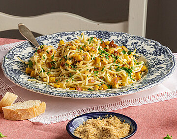 Spaghetti mit kleinen Tofuwürfeln und Streukäse und Kräutern auf 2 Tellern und Tischdekoration.