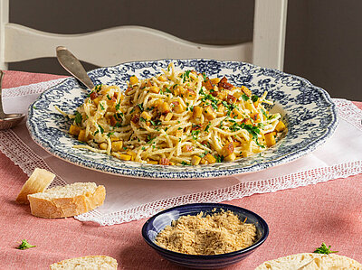 Spaghetti mit kleinen Tofuwürfeln und Streukäse und Kräutern auf 2 Tellern und Tischdekoration.