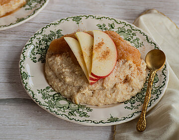 Tofu-Grießcreme mit Zimt-Apfelkompott Tofu-Grießbrei auf einem Teller mit Apfelscheiben und Apfelmus mit Zimt mit Tischdekoration.