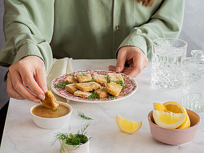 Gelbe Tofuwürfel auf einem Teller mit Zitrone und Gurke und Dekoration.