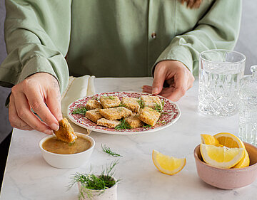 Gelbe Tofuwürfel auf einem Teller mit Zitrone und Gurke und Dekoration.