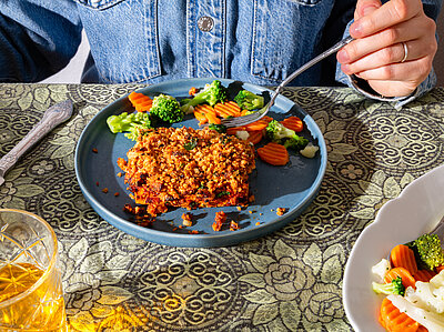 Tofugehacktes an gemischetes Gemüse auf einem blauen Teller mit Tischdekoration.