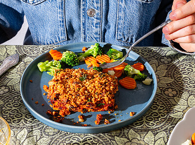 Tofugehacktes an gemischetes Gemüse auf einem blauen Teller mit Tischdekoration.