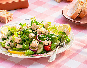 2 Teller mit Sojawürfeln auf Salat mit Zitrone und Brot mit Tischdekoration.