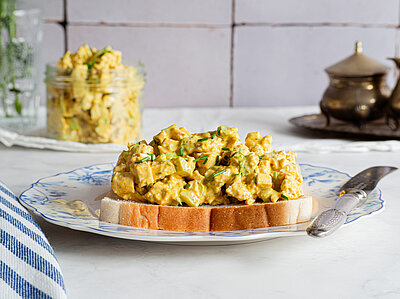 Tofu in gelber, dicker Sauce auf Toast auf einem Teller von Dekoration.