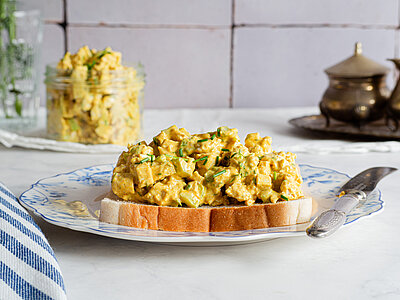 Tofu in gelber, dicker Sauce auf Toast auf einem Teller von Dekoration.