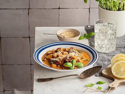 Tofuwürfel in Tomatensauce auf einem Teller, jemand streut geriebenen Käse darüber.