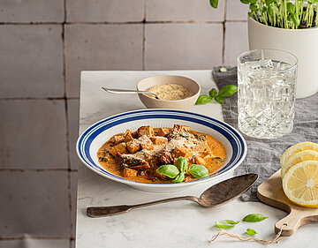 Tofuwürfel in Tomatensauce auf einem Teller, jemand streut geriebenen Käse darüber.