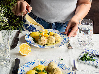 Gelbe Klopse an Kartoffeln mit Gelber Sauce und Zitrone auf Tellern mit Dekoration.