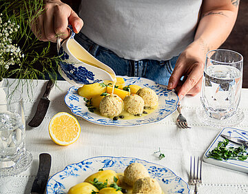 Gelbe Klopse an Kartoffeln mit Gelber Sauce und Zitrone auf Tellern mit Dekoration.