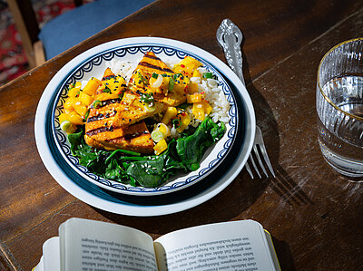 Gegrillter Tofu auf Salat und Reis und Mango in einem Teller mit Tischdekoration.