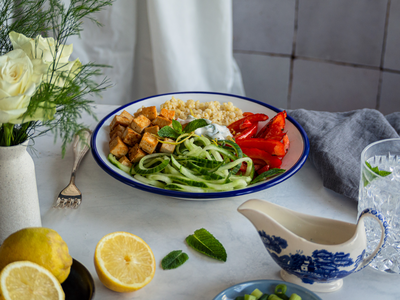 Bulgur, Tofuwürfel, Gurkenstreifen, und Paprika auf einem Teller mit Zitrone und Tischdekoration.