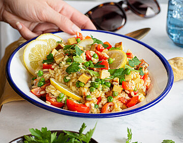 Paella mit Tofustückchen und buntem Gemüse und Zitrone auf einem Teller mit Tischdekoration.