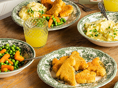 Mehrere Teller mit Tofu Nuggets, Kartoffelpüree und Erbsen und Möhren mit Tischdekoration.