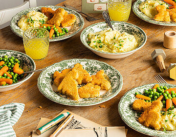 Mehrere Teller mit Tofu Nuggets, Kartoffelpüree und Erbsen und Möhren mit Tischdekoration.