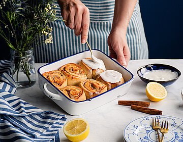 6 Zimtschnecken in einer Schale mit Zuckerguß mit Tischdekoration.