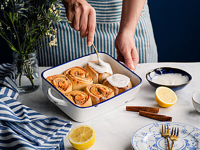 6 Zimtschnecken in einer Schale mit Zuckerguß mit Tischdekoration.