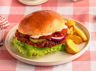 Teller mit Burger und Dipp auf kariertem Tischtuch.