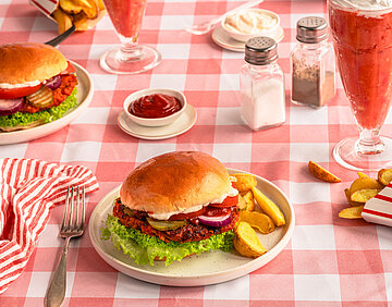 Teller mit Burger und Dipp auf kariertem Tischtuch.