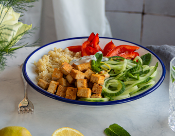 Tofu-Bulgur-Bowl Bulgur, Tofuwürfel, Gurkenstreifen, und Paprika auf einem Teller mit Zitrone und Tischdekoration.