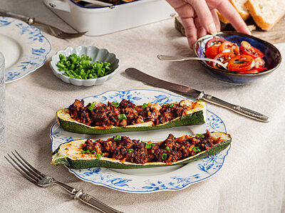 Zucchini gefüllt mit angebratenem Tofu auf einem Teller mit Tomaten und Tischdekoration.