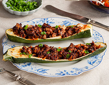 Gevüllte Zucchini Zucchini gefüllt mit angebratenem Tofu auf einem Teller mit Tomaten und Tischdekoration.