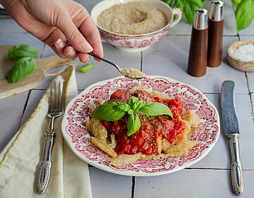 Nudeln mit Tomaten-Stückchen und roter Sauce mit Tischdekoration, Streukäse wird darüber gestreut.