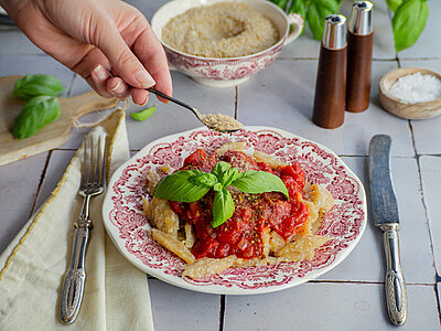 Nudeln mit Tomaten-Stückchen und roter Sauce mit Tischdekoration, Streukäse wird darüber gestreut.