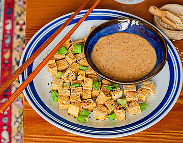 Helle Tofustückchen mit Lauch auf einem Teller mit Dip und Tischdekoration.