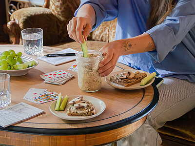 Helle Creme in einem Glas neben 2 Tellern mit Brot und Creme mit Tischdekoration.