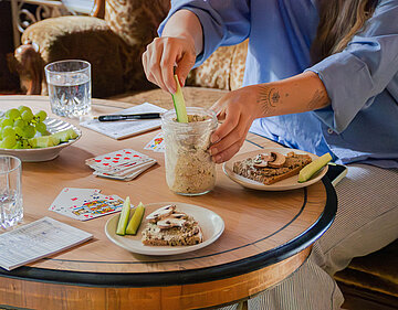 Helle Creme in einem Glas neben 2 Tellern mit Brot und Creme mit Tischdekoration.