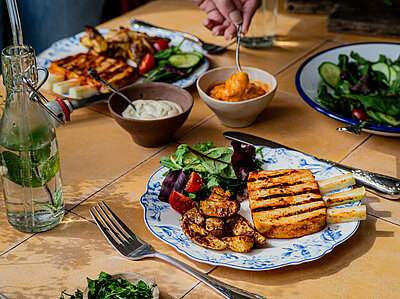 Gegrillte Tofu-Rippchen und Kartofellspalten mit Salat auf 2 Tellern mit Tischdekoration. 