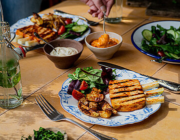 Gegrillte Tofu-Rippchen und Kartofellspalten mit Salat auf 2 Tellern mit Tischdekoration. 