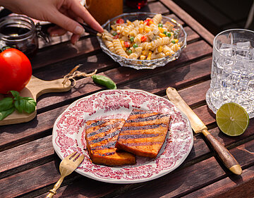 Tisch mit Tellern von Tofu, Nudeln, Oliven, Tomaten und Dekoration.