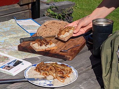 Helle Creme mit Zwiebeln und Tofustückchen auf einem Teller und Broten, die von einer Hand gehalten werden mit Tischdekoration.