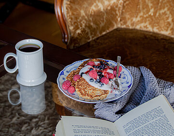 Pancakes auf einem Teller mit Himbeeren und Heidelbeeren auf einem Tisch mit Dekoration.
