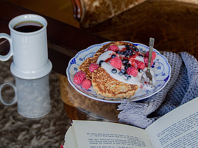 Pancakes auf einem Teller mit Himbeeren und Heidelbeeren auf einem Tisch mit Dekoration.