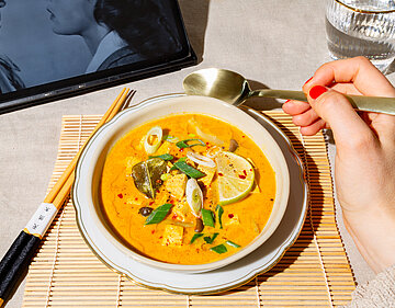 Gelbe Suppe mit Tofuwürfeln, Lauch und Zitrone auf einem Teller mit Dekoration.