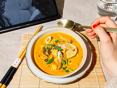 Gelbe Suppe mit Tofuwürfeln, Lauch und Zitrone auf einem Teller mit Dekoration.