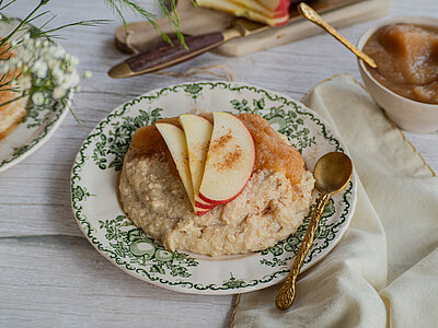 Tofu-Grießbrei auf einem Teller mit Apfelscheiben und Apfelmus mit Zimt mit Tischdekoration.
