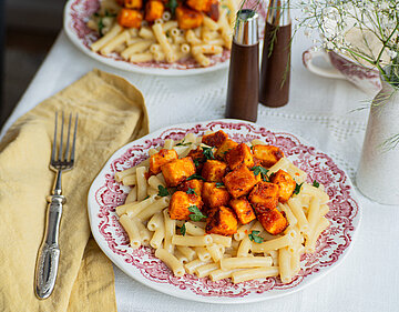 Zwei Teller auf einem Tischtuch mit Nudeln und gebratenem Tofu.