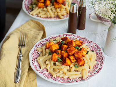Zwei Teller auf einem Tischtuch mit Nudeln und gebratenem Tofu.