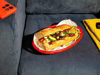 Ein mit Tofu und gemischtem Salat belegtes Baguette auf einm Teller auf einem Sessel.