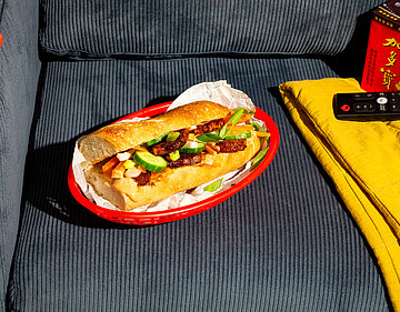 Banh-Mi-Sandwich Ein mit Tofu und gemischtem Salat belegtes Baguette auf einm Teller auf einem Sessel.