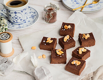 Erdnuss Brownies auf einer Tischdecke mit Dekoration.