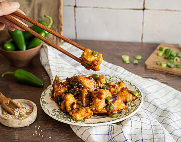 Knusprig scharfer Tofu Gebackene Tofuwürfel in einer glänzenden Soße mit Sesam auf einem Teller mit Dekoration.