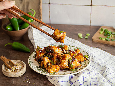 Gebackene Tofuwürfel in einer glänzenden Soße mit Sesam auf einem Teller mit Dekoration.