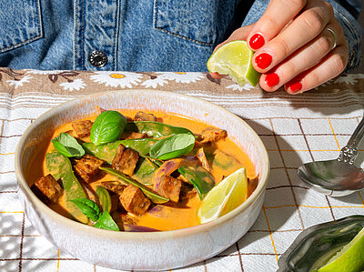 Eine Schüssel mit einem Curry auf einem Tischtuch mit Deko.