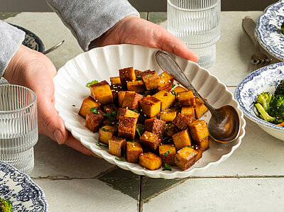 Einige Teller mit Räuchertofu und Gemüse auf einem Tisch, ein Teller wird in die Kamera gehalten. 