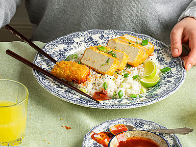 Aufgeschnittene Tofuscheibe auf Reis auf einem Teller mit Tischdekoration.
